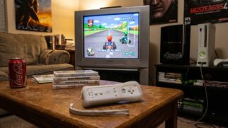 Cenário de jogos retrô com consoles PlayStation 3 e Xbox 360 ao lado de uma televisão antiga transmitindo uma corrida de videogame.