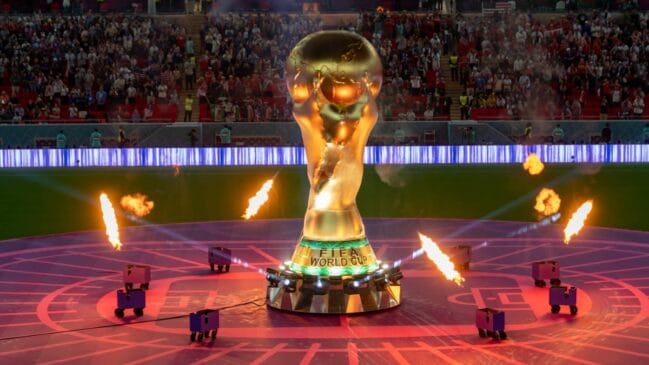 Escultura do troféu da Copa do Mundo em exposição no centro de um estádio durante cerimônia esportiva.