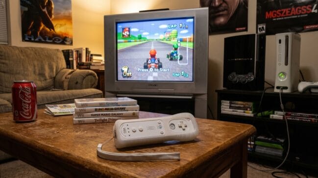 Cenário de jogos retrô com consoles PlayStation 3 e Xbox 360 ao lado de uma televisão antiga transmitindo uma corrida de videogame.