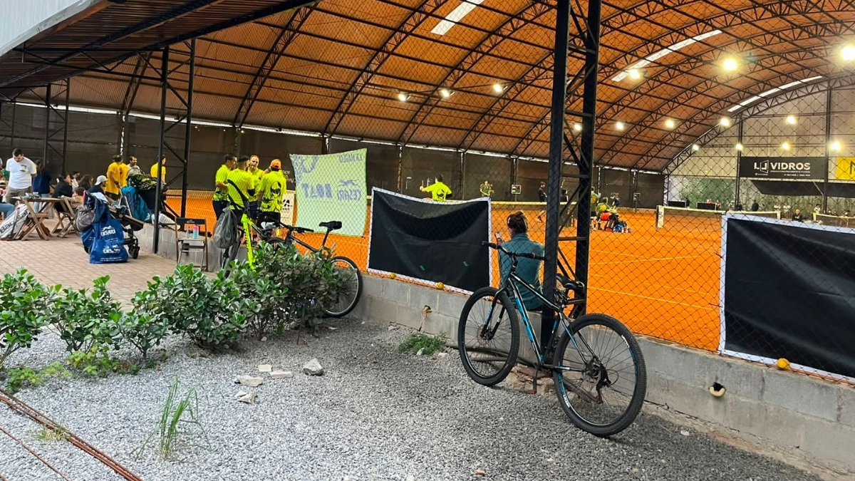 Bicicleta encostada em uma tela de proteção com uma quadra de tênis de saibro visível ao fundo.