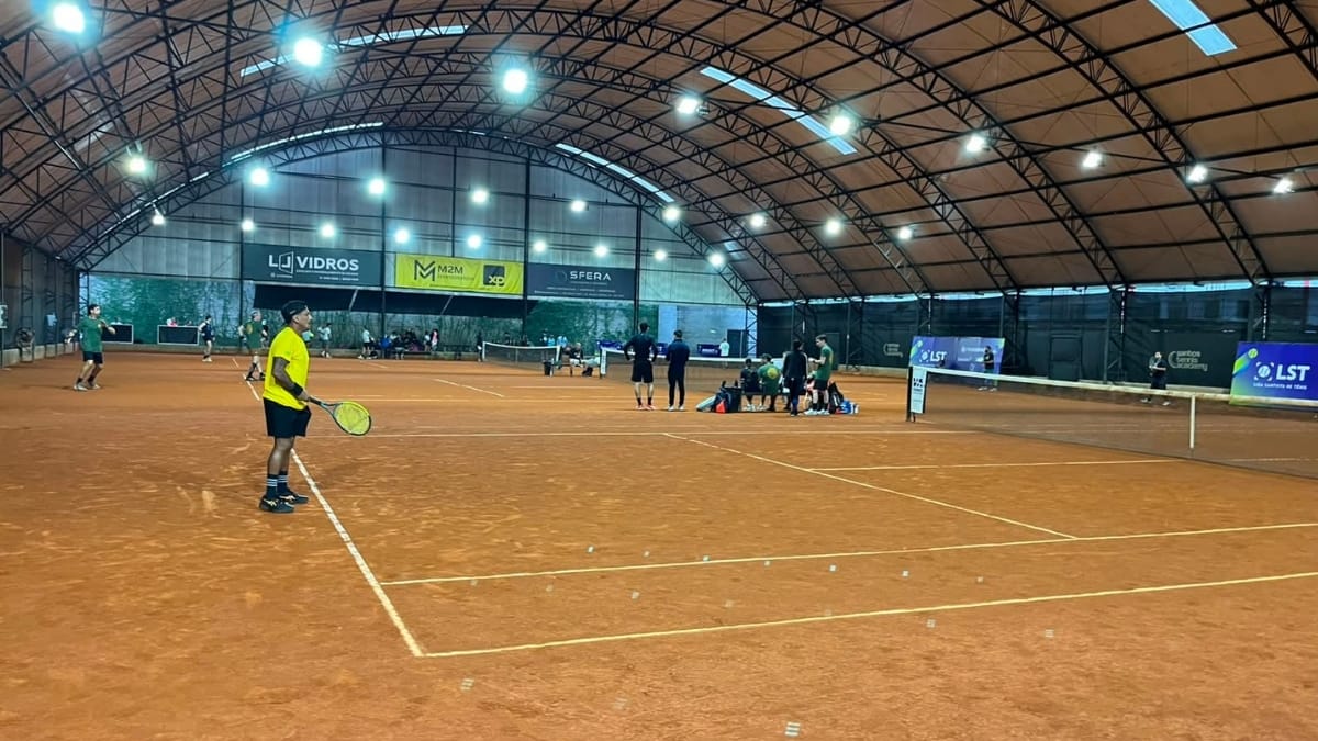 Jogador de tênis em quadra de saibro, visto de costas, preparando-se para realizar o saque.