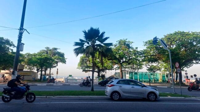 Avenida da Praia de Santos com arvores ao fundo, um carro e uma moto passando pela rua