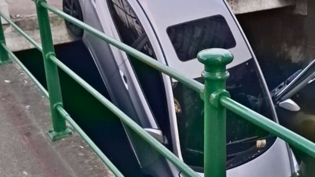 Imagem do veículo prata pendurado na mureta do Canal 5, em Santos