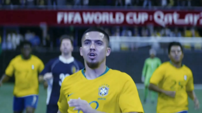A imagem é um frame de um filme de ficção que simula uma partida de futebol. Em primeiro plano, centralizado, aparece um jogador fictício com feições que lembram o atleta Gabriel Jesus. Ele está de frente, com o corpo ligeiramente voltado para a esquerda e o olhar fixo para o alto, com uma expressão de surpresa ou espanto, mantendo a boca aberta. Ele tem pele parda, cabelo curto raspado nas laterais e um cavanhaque desenhado. Veste o uniforme da Seleção Brasileira: uma camisa amarela com gola verde e o escudo da CBF estampado no peito. Ao fundo, com desfoque moderado, há outros jogadores em campo. À esquerda e à direita do protagonista, aparecem dois atletas também com a camisa amarela do Brasil. Mais atrás, do lado esquerdo, nota-se um jogador com uniforme azul-escuro. Ao fundo, no canto direito, o goleiro aparece com uniforme verde claro, posicionado perto da trave. Na parte superior da imagem, acima da linha do gramado, destaca-se uma placa publicitária vermelha na arquibancada com a inscrição em letras brancas: "FIFA WORLD CUP Qatar". A iluminação simula a de refletores de um estádio de futebol à noite.