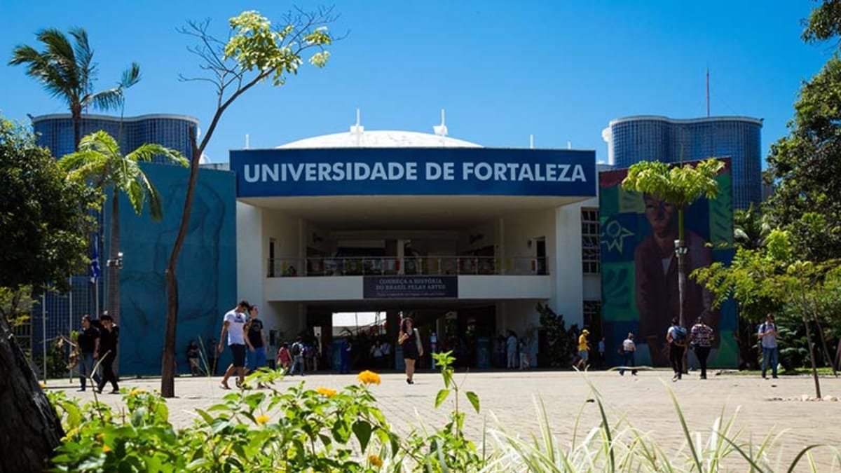 Fachada da Universidade de Fortaleza (Unifor) em dia ensolarado, com estudantes circulando e vegetação em primeiro plano, destacando o ambiente de aprendizado.