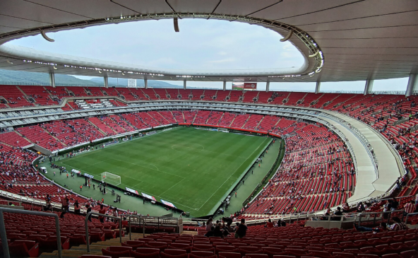 Vista panorâmica de um grande estádio de futebol com arquibancadas vermelhas e gramado ao centro.
