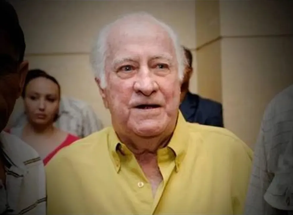 Fotografia horizontal em primeiro plano focando um homem idoso de cabelos brancos vestindo camisa de botão amarela clara