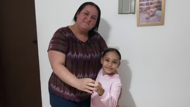 Uma mulher abraçada com uma criança com diversas medalhas e uma roupa de ballet