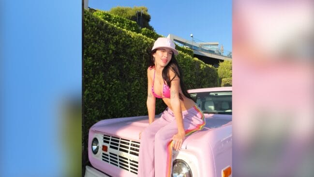 Uma mulher sentada em um capo de carro cor de rosa