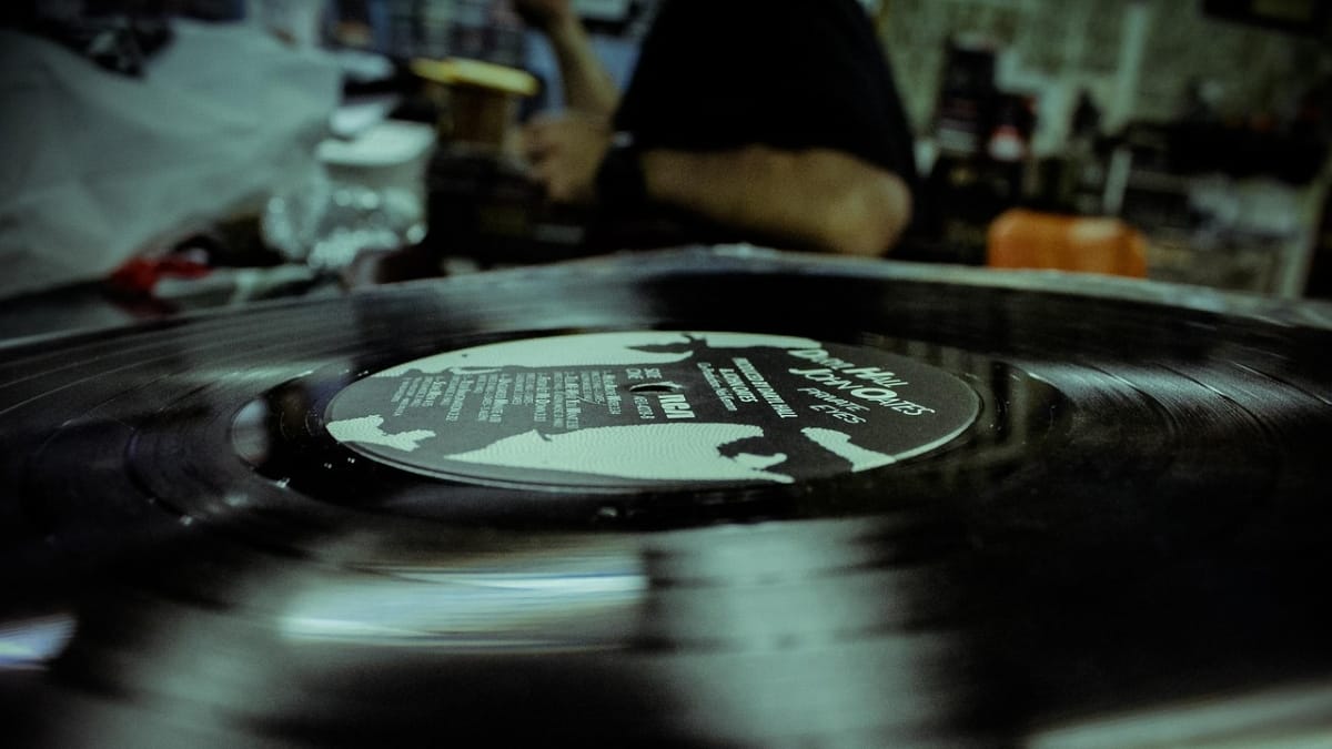 Disco de vinil do álbum "Private Eyes" da dupla Hall & Oates girando em uma vitrola, com ambiente de loja de discos ao fundo, destacando a cultura do colecionismo musical.