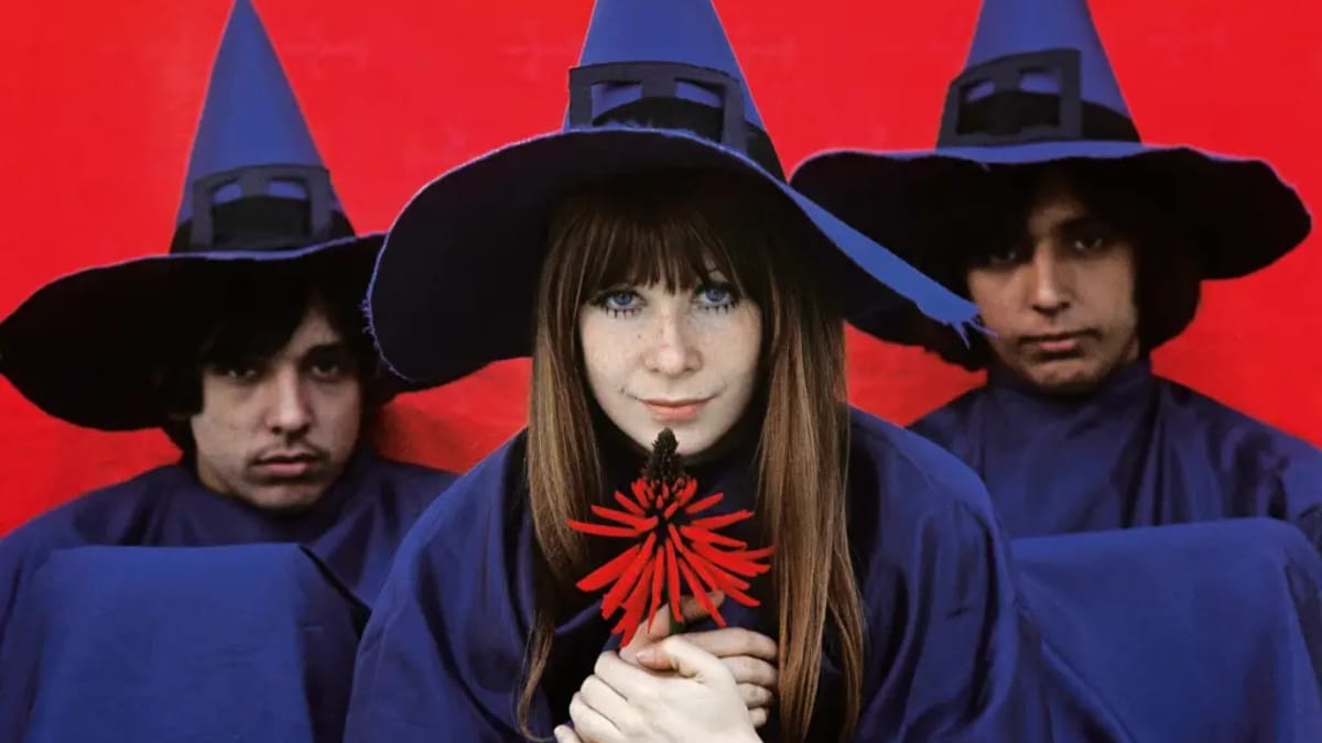 Rita Lee, Arnaldo Baptista e Sérgio Dias do grupo Os Mutantes, vestindo trajes de feiticeiros, com fundo vermelho vivo, simbolizando a vanguarda e a psicodelia da Tropicália no rock brasileiro.