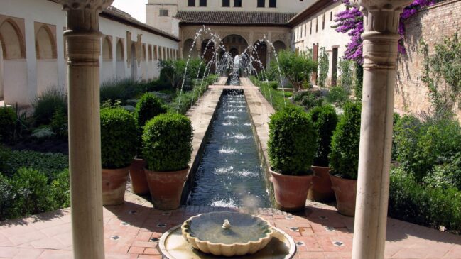 Pátio interno com uma longa fileira de fontes de água cruzadas e arbustos verdes esculpidos no Palácio de Generalife em Granada