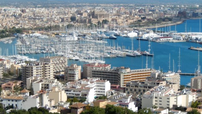 Vista panorâmica aérea de uma marina repleta de veleiros e iates brancos em Palma de Maiorca, com prédios costeiros em primeiro plano