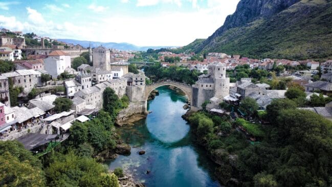 Fotografia horizontal registrando a icônica ponte antiga Stari Most sobre as águas esverdeadas do rio Neretva em Mostar