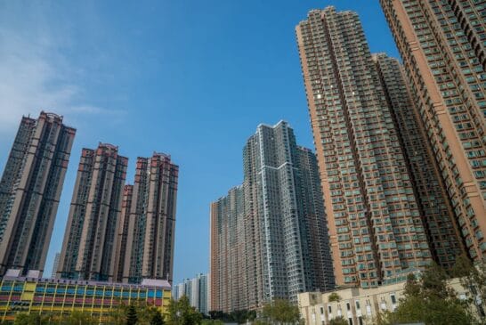 Conjunto de edifícios residenciais altos em área urbana densamente povoada, fotografados de baixo para cima sob céu azul e sem nuvens.