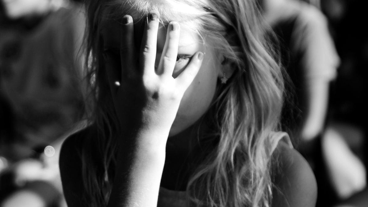 Criança com o rosto tapado por mãos