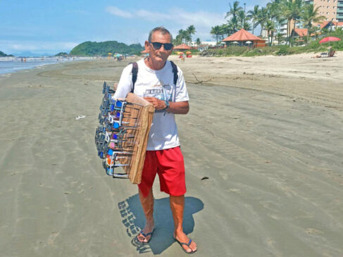 Jonas caminha e mostra os óculos de sol aos turistas, todos os dias, na praia do centro, em Itanhaém