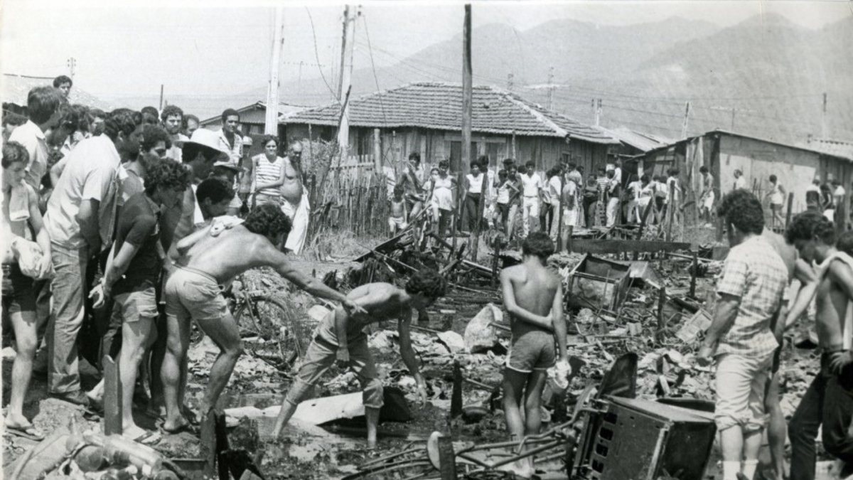 Homens retiram objetos pessoais em meio aos destroços após incêndio na Vila Soco, em Cubatão (SP). (Foto: Matuiti Mayezo/Folhapress/25/02/1984)