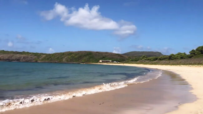 A faixa de areia é cercada por montanhas e tem uma água bem clara