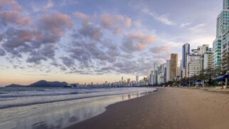 A paisagem urbana é marcada por modernos arranha-céus que contrastam com o azul do mar, criando um visual único