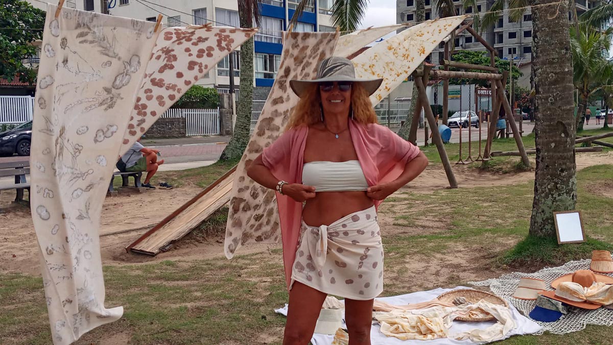Artista mostra chapéus e lenços com estampas de flores em um varal, na orla do Praião, em Itanhaém