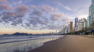 A paisagem urbana é marcada por modernos arranha-céus que contrastam com o azul do mar, criando um visual único