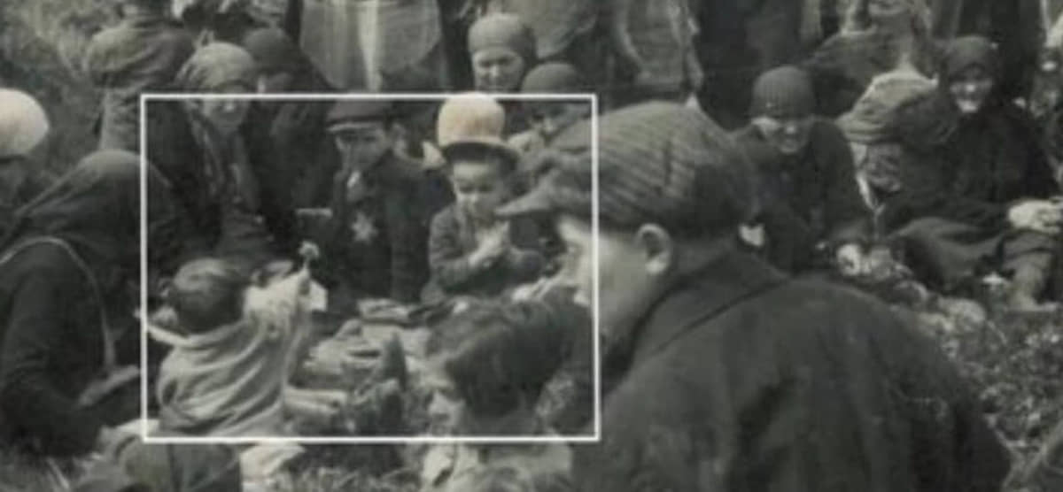 Criança oferece flor para outra criança antes de entrarem na câmara de gás