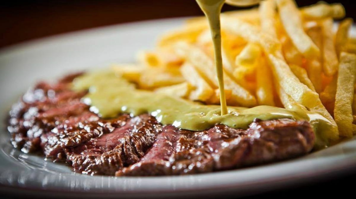 O prato servido é um clássico francês entrecôte, acompanhado de salada verde, batatas fritas crocantes e um molho secreto