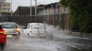 Carros enfrentam rua alagada após chuvas fortes