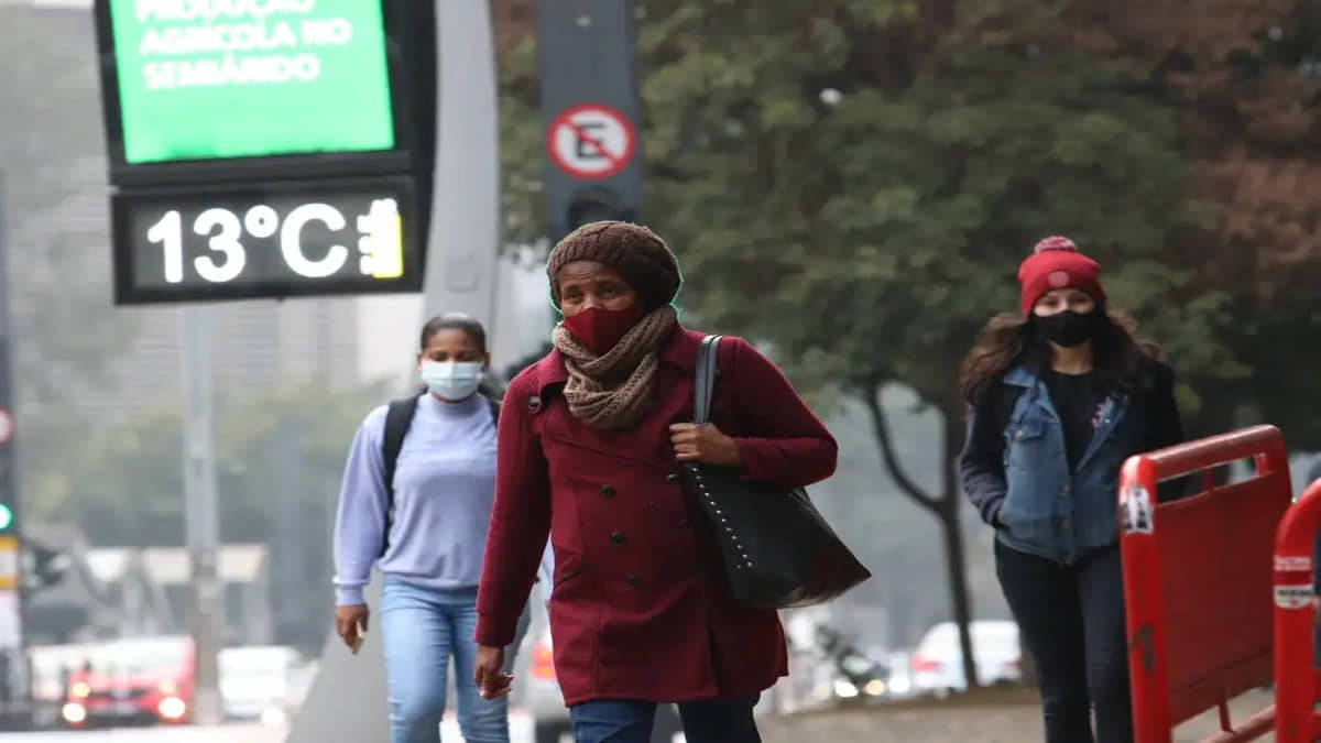 Pessoas andam na rua durante chuva fraca e frio