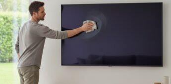 Homem limpa a tela da sua TV na sala de casa