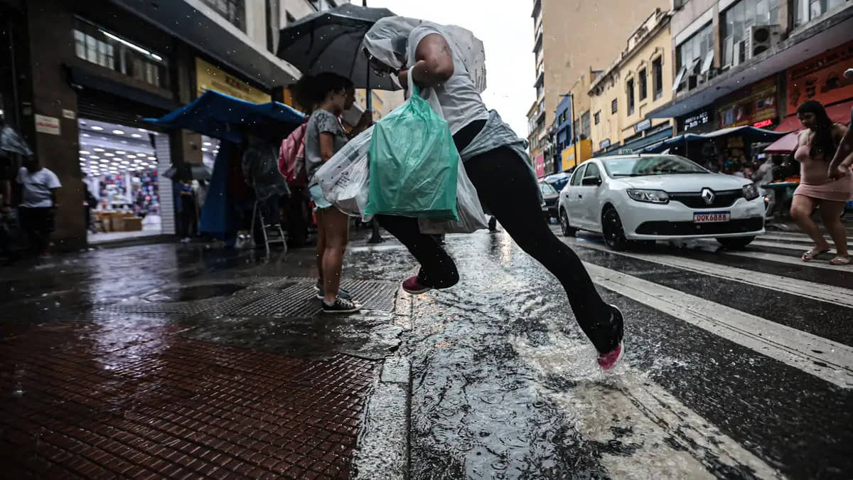 Homem tenta pular de poça de água que se formou durante chuva na rua