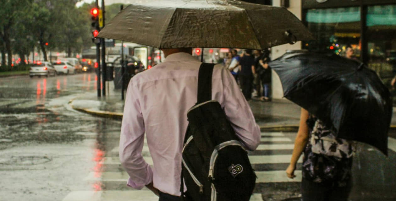 Homem e mulher atravessam a rua em dia chuvoso com seus guarda-chuvas