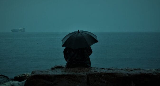 Mulher observa a chuva na beira do mar em cidade do litoral