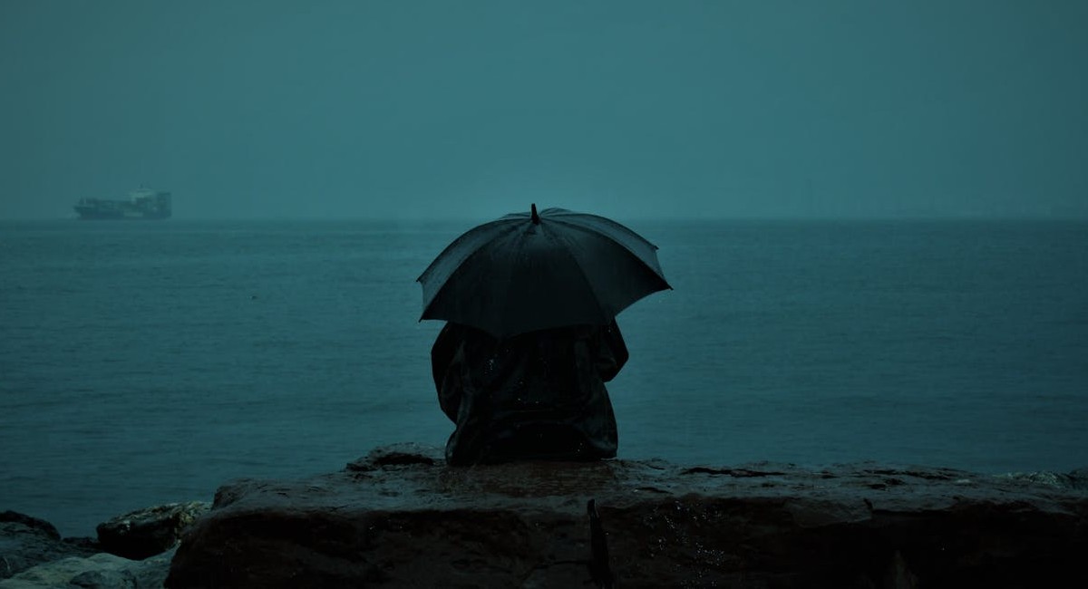 Mulher observa a chuva na beira do mar em cidade do litoral