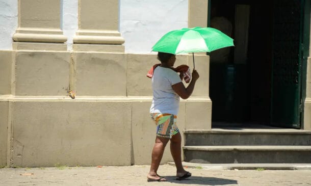 Mulher segura sombrinha para fugir do sol forte em dia de calor intenso no Brasil