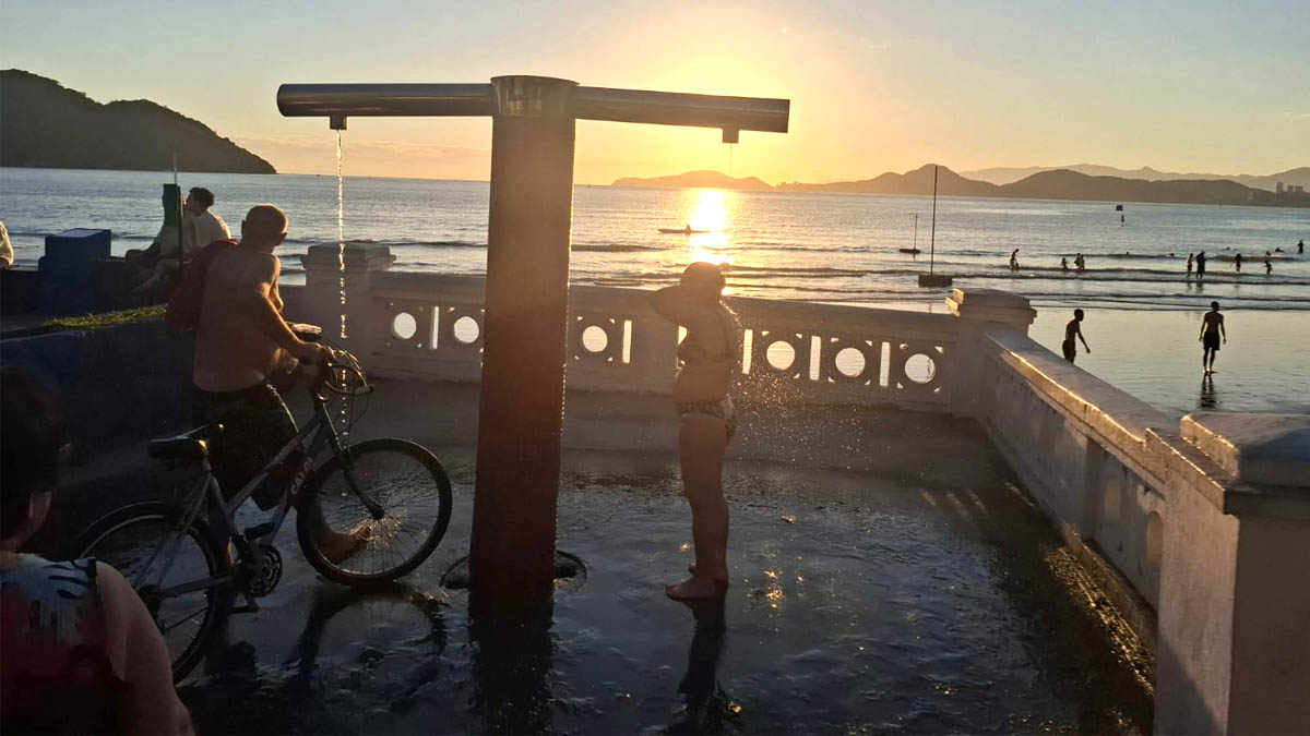 Pessoas se refrescam nos chuveirinhos da praia de Santos em uma tarde de calor