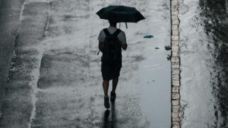 Rapaz caminha segurando um guarda-chuva em dia nublado