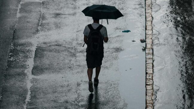 Rapaz caminha segurando um guarda-chuva em dia nublado
