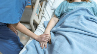 Médico segura a mão de paciente em coma no leito hospitalar