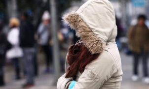 Mulher se protege do frio na rua durante queda nos termômetros no outono