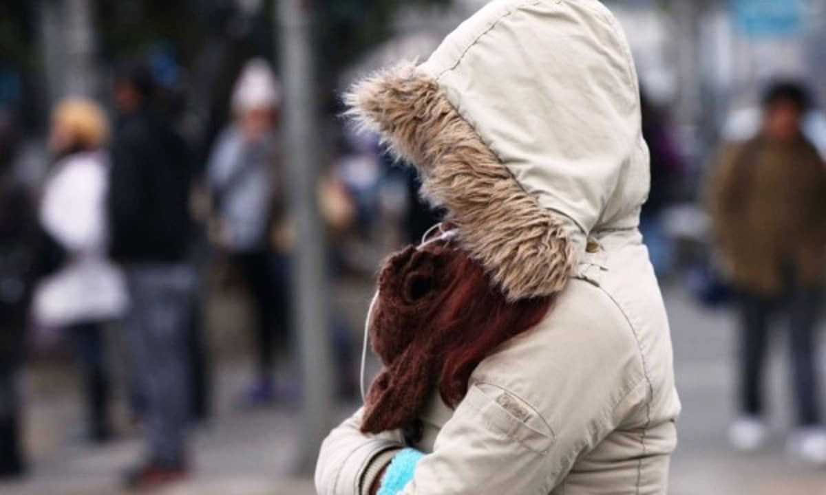 Mulher se protege do frio na rua durante queda nos termômetros no outono