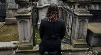 Mulher ajoelhada diante de sepultura em cemitério tradicional da cidade