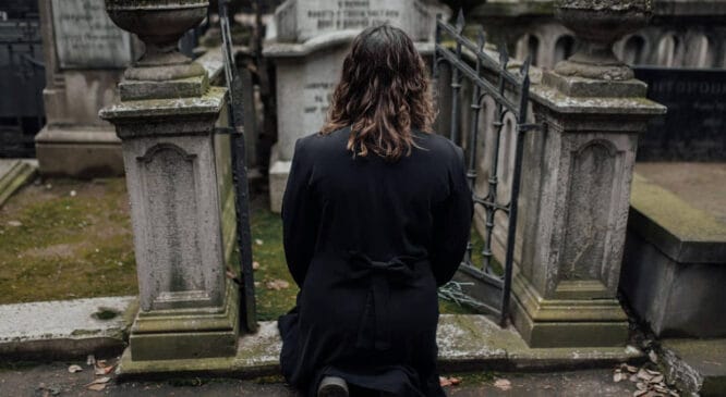 Mulher ajoelhada diante de sepultura em cemitério tradicional da cidade