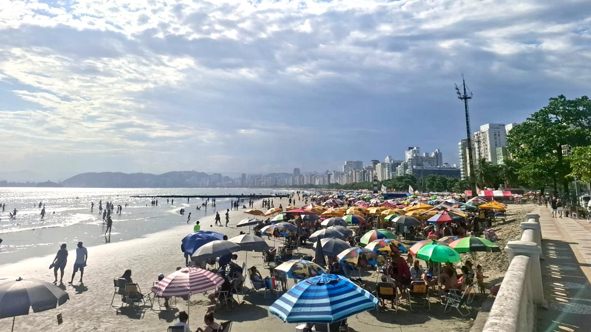 Praia de Santos lotada em uma tarde de 2026 com sol forte e muitos turistas