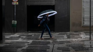 Mulher caminha de guarda-chuva em tarde úmida e cinza